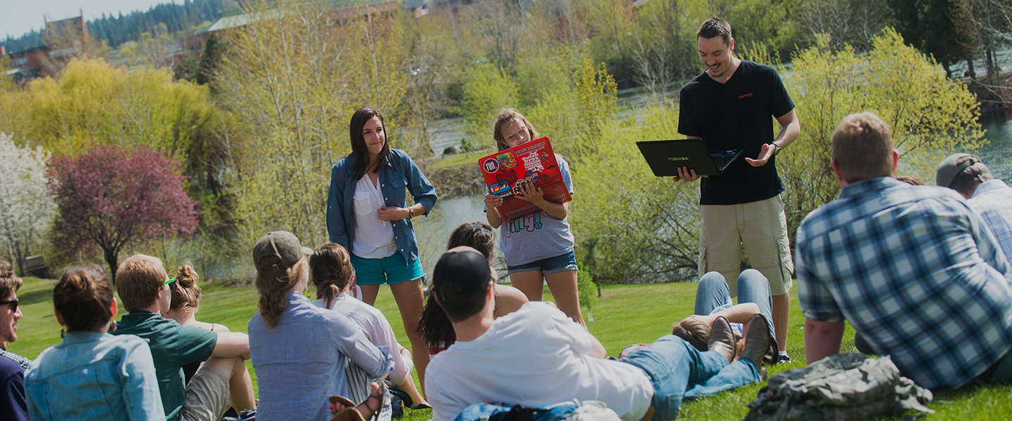 Students give a presentation on the lawn in front of Lake Arthur