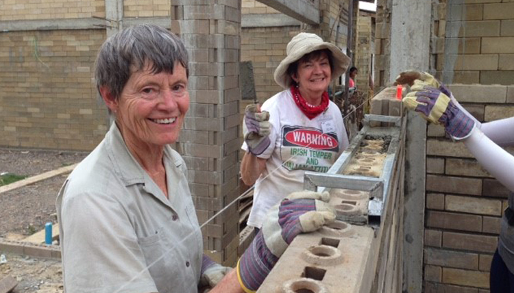 Women smiling as they place bricks in a wall