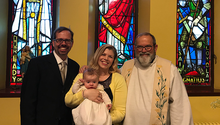 baby with parents and priest in Catholic church with stained glass windows