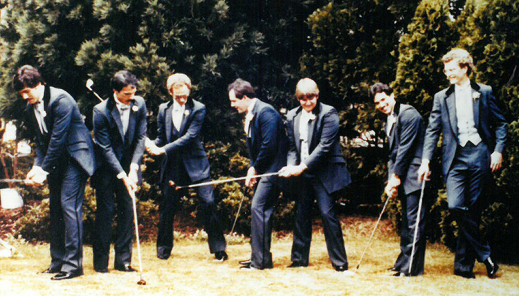 seven male friends post with golf clubs in a 1980s wedding photo