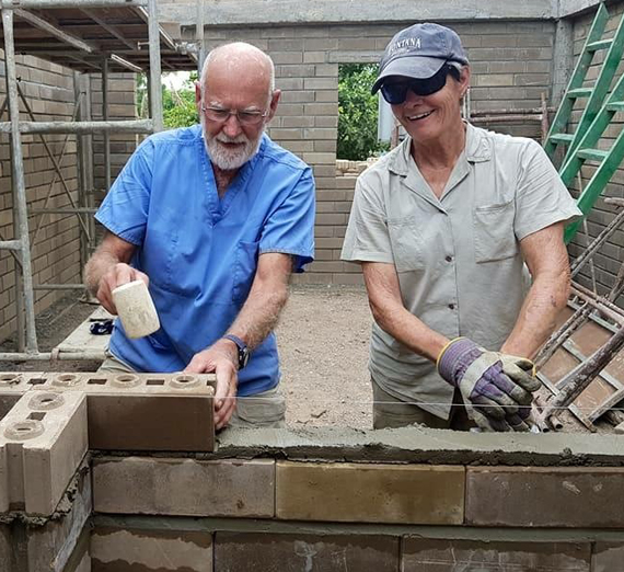 Husband and wife volunteering by laying bricks for a house 