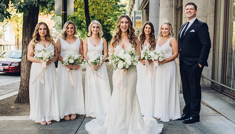 bride surrounded by bridesmaids in white and groom