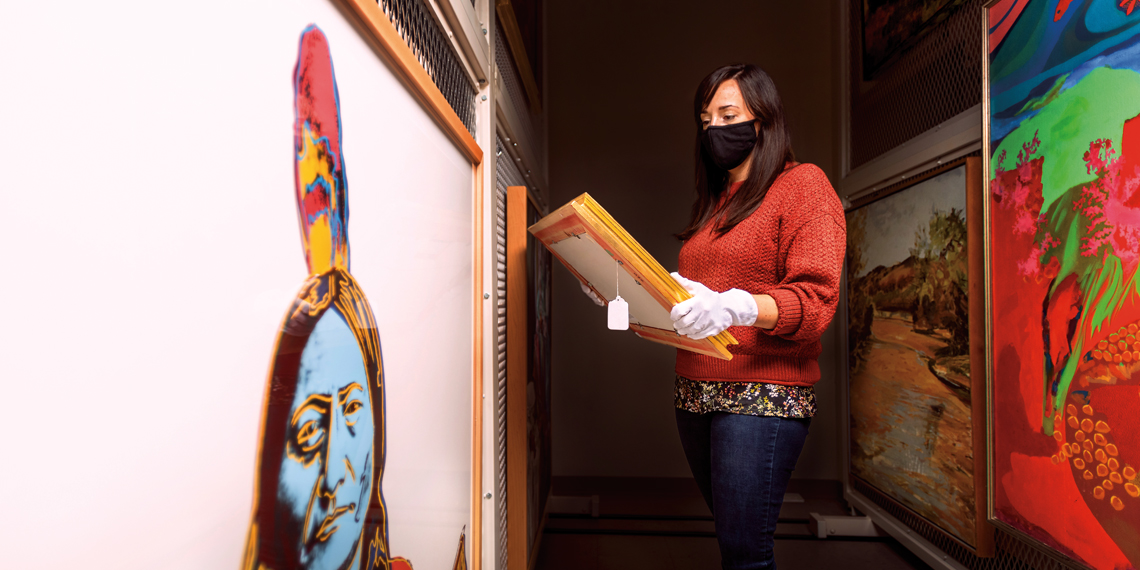 staff member pulls art from storage, with Andy Warhol's Sitting Bull in foreground