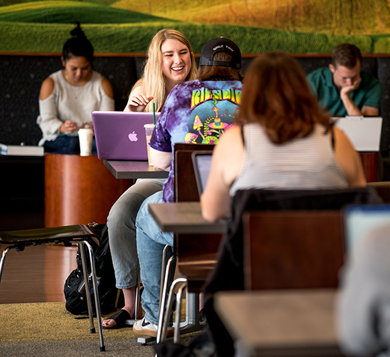 Students studying at tables in Hemmingson. The photo is focused on one student laughing.