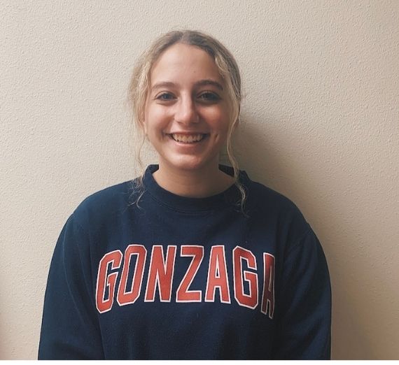 A photo of a current Gonzaga student. She is smiling and is wearing a navy long sleeved shirt that says GONZAGA in red letters.