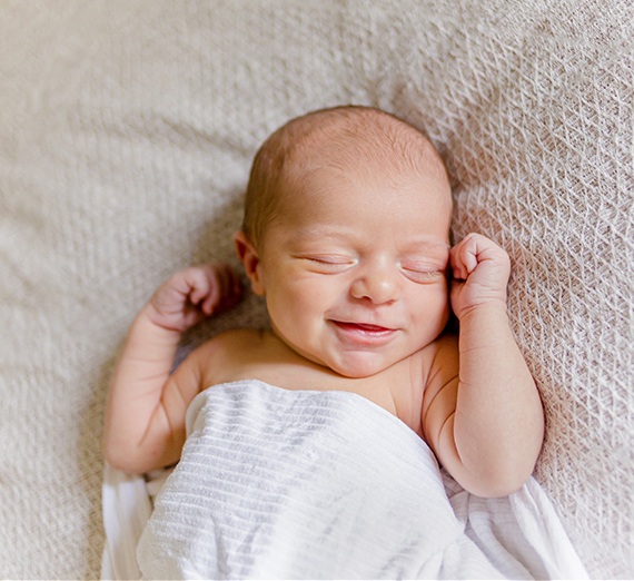 A baby smiles while wrapped in a white blanket. 