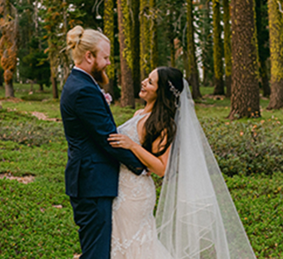 Man and women look at each other in a forest in wedding outfits. 