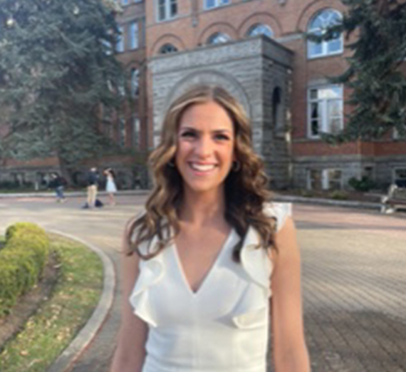 A woman in graduation cap and gown holds up her degree and smiles