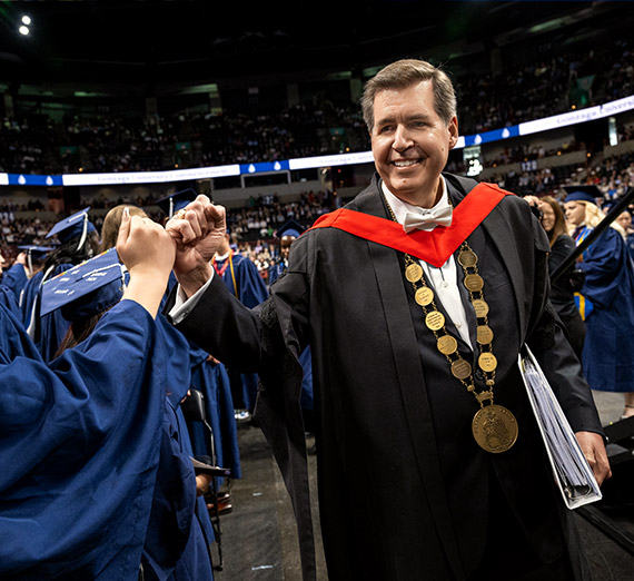 A man in commencement regalia holds up his degree with Gonzaga University written on it