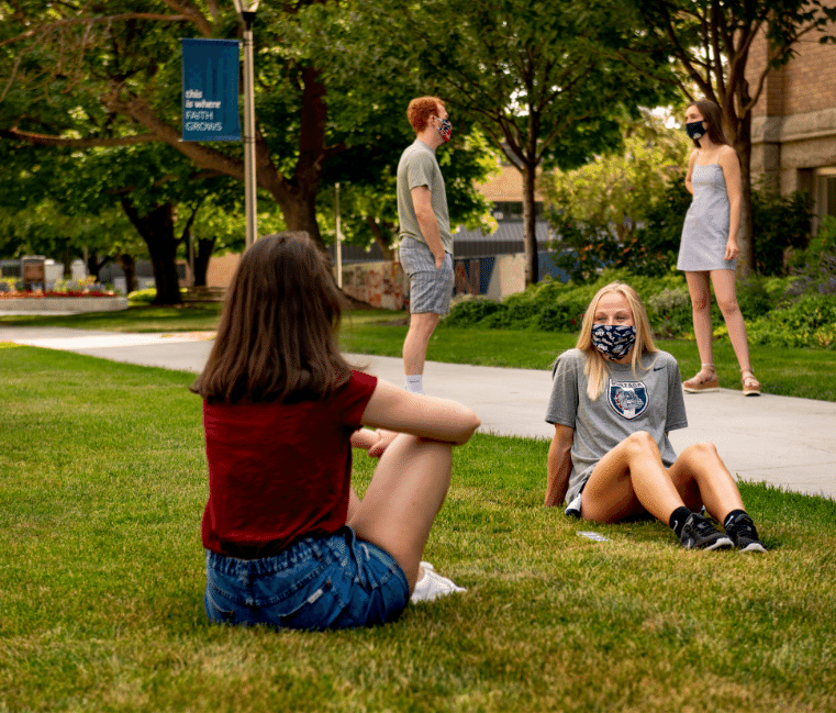 4 masked students on campus talking with each other