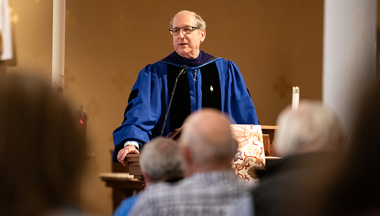 A man in a blue robe stands at a podium in front of a crowd. A man in a blue robe stands at a podium in front of a crowd.