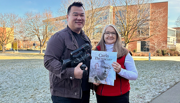 Clement Lye stands holding a camera next to Kristine Hoover holding a magazine. Clement Lye stands holding a camera next to Kristine Hoover holding a magazine.