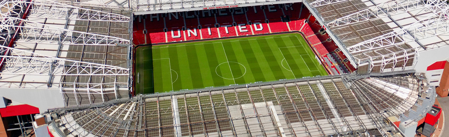 photo looking down at Manchester united stadium. Shows green soccer field surrounded by red seats with 