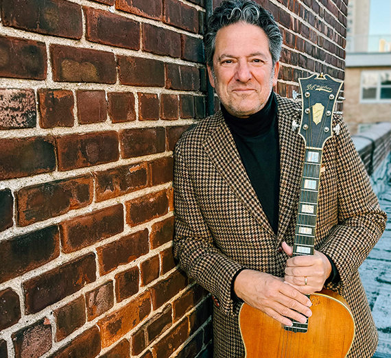 John Pizzarelli with his guitar smiling.