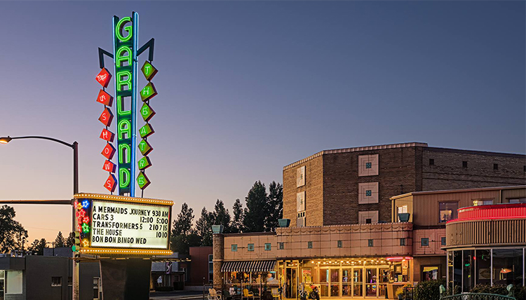 The neon sign of the Garland Theater is lit up at night and lists the movies being shown. The neon sign of the Garland Theater is lit up at night and lists the movies being shown.