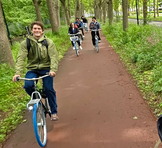several students ride bicycles down a forested trail