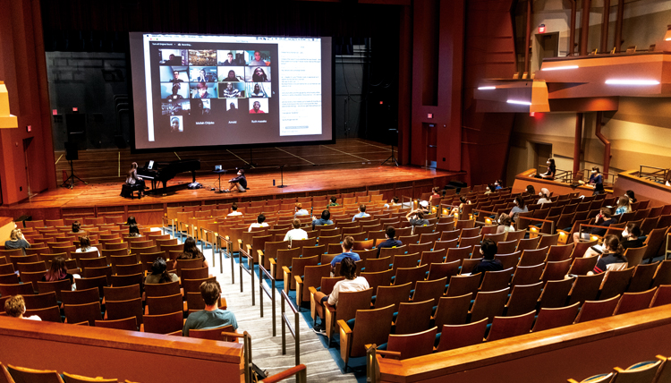 students seated far apart in Woldson Theatre with performance on screen students seated far apart in Woldson Theatre with performance on screen