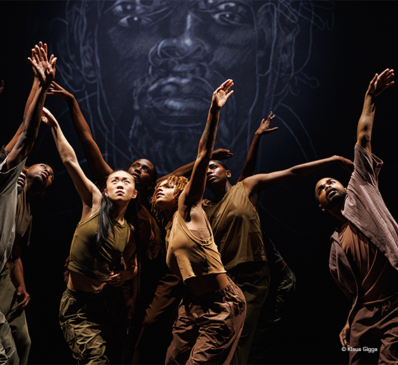 A.I.M by Kyle Abraham contemporary dance company performers in dramatic lighting, reaching upward in a powerful ensemble pose.