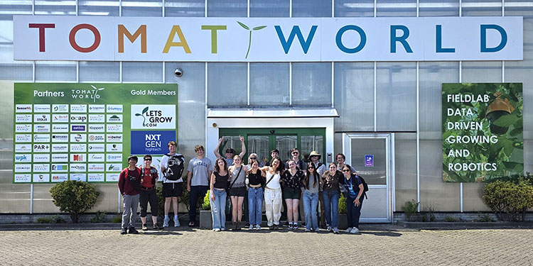 delft 2026-0526 tomatoworld group-bd A row of students pose in front of a sign saying Tomatoworld