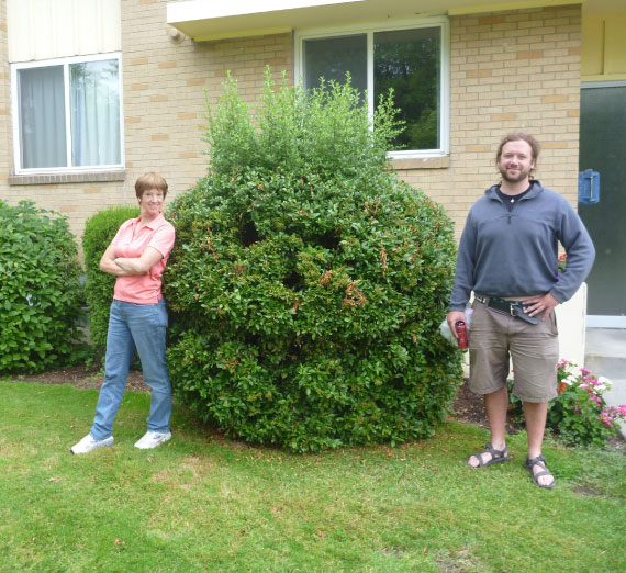scholarship-jimmy-magnuson-silly-bush Two individuals pose with a bush pruned into smiling face.