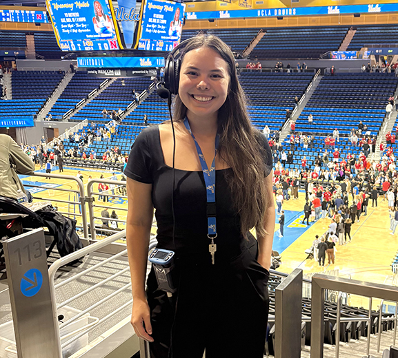 Woma wearing black top and pants standing with UCLA basketball court in the background.