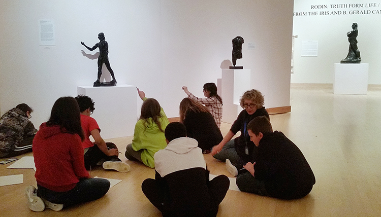 Middle school students sit on the floor of the museum discussing bronze art on display. Middle school students sit on the floor of the museum discussing bronze art on display.