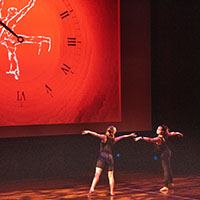 Two dancers in front of large clock image. Two dancers in front of large clock image.