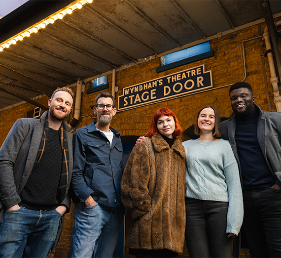 Five actors posed in a line in front of the Wyndam's Theatre Stage Door.