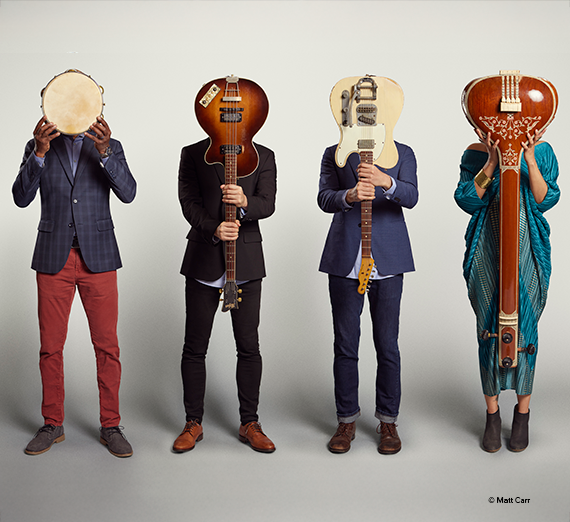 American Patchwork Quilt posed with the body of their instruments in front of their faces with the instruments neck toward the ground. 