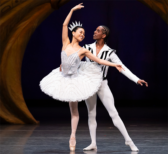 Two ballet dancers in white costumes in a pose together.
