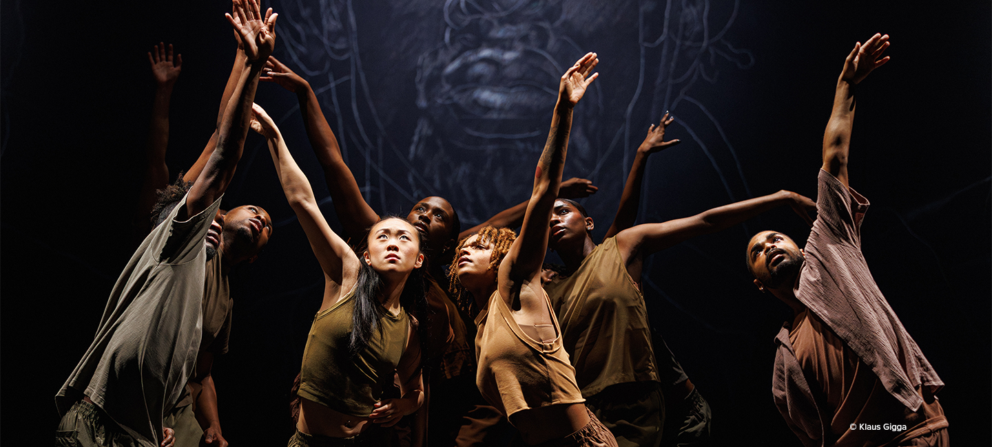 A.I.M by Kyle Abraham contemporary dance company performers in dramatic lighting, reaching upward in a powerful ensemble pose.