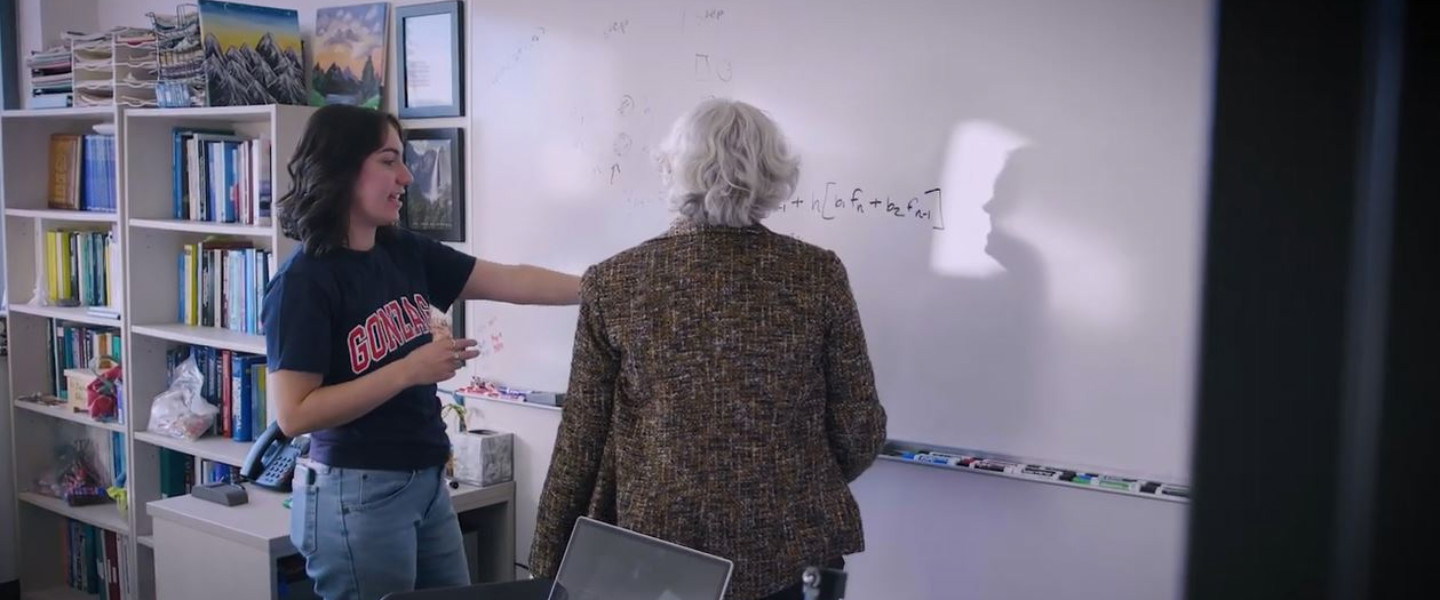 A student and faculty member discussing an equation at a white board. 