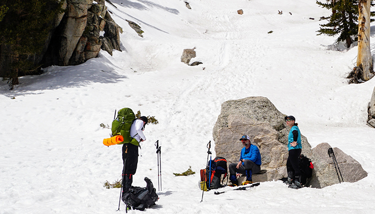 hikers rest on a rock in the snow on the mountain side hikers rest on a rock in the snow on the mountain side