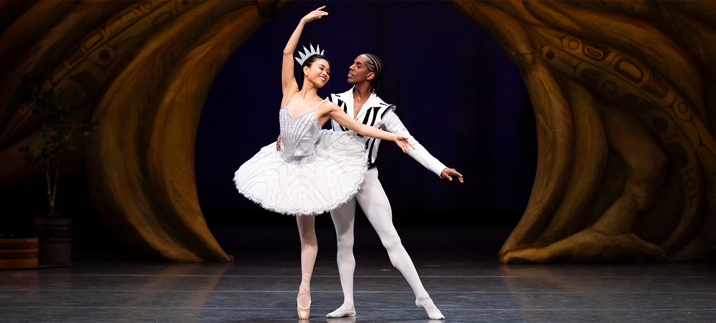 Two ballet dancers in white costumes in a pose together.