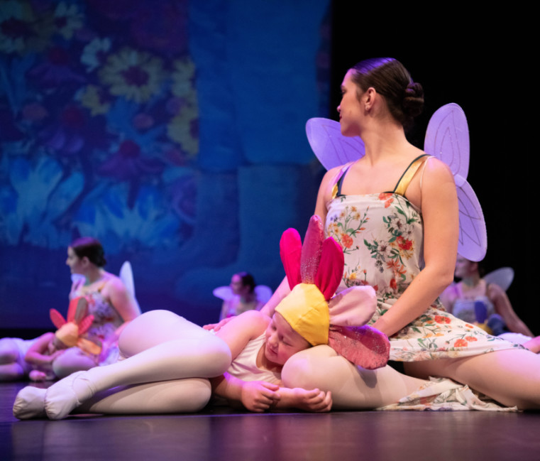 Actors from the Gonzaga University production of Thumbelina dressed in fairy costumes seated on stage with other actors dressed as flowers sleeping on the fairy's knees. 