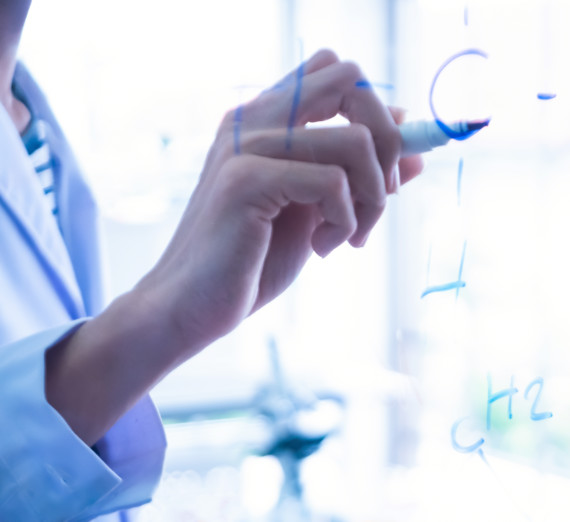 A hand writing molecules on a white board.