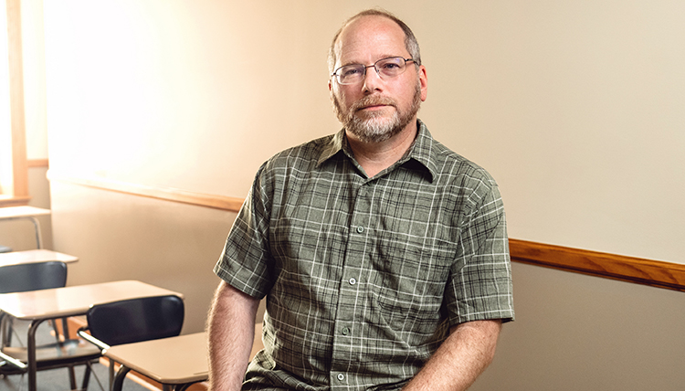 A man sits on the edge of a desk