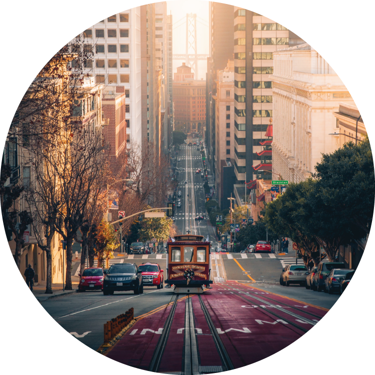 A traditional trolley rolls down the center of the road sandwiched between vast buildings on either side in downtown San Francisco. A traditional trolley rolls down the center of the road sandwiched between vast buildings on either side in downtown San Francisco.