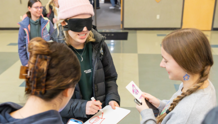 Two girls describing a picture to a blindfolded person who is trying to draw what they see Two girls describing a picture to a blindfolded person who is trying to draw what they see
