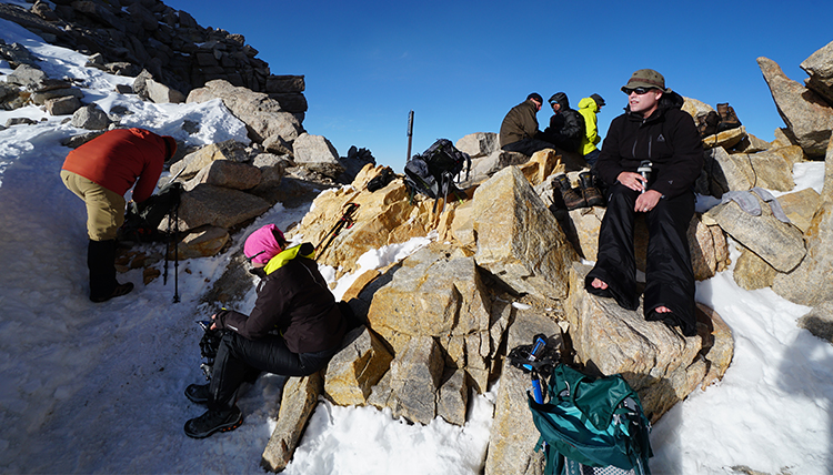 hikers take a rest break on rocks in the snow on the mountain hikers take a rest break on rocks in the snow on the mountain