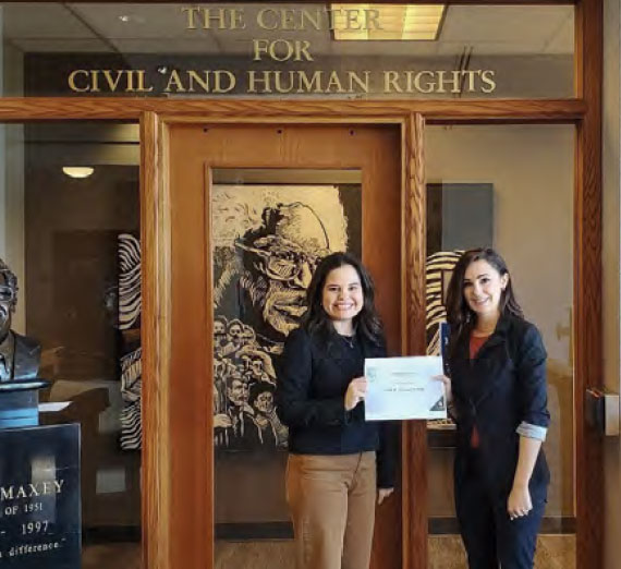 Two women stand smiling in front of a door labeled 