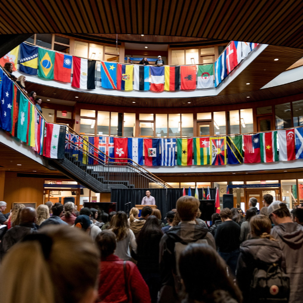 Crowd of students gathered in the Hemmingson Center Rotunda listening to a speaker. Hemmingson is decorated with different countries' flags each representing a member of our campus community.