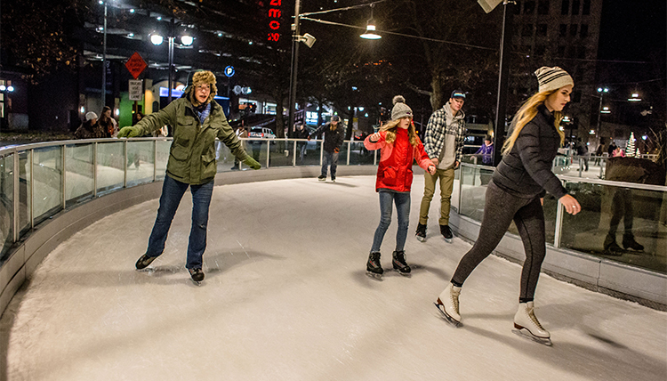 Three people ice skate around a corner on the ice ribbon. Three people ice skate around a corner on the ice ribbon.
