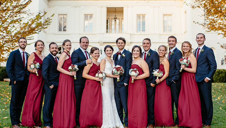 large wedding party in crimson attire outside mansion large wedding party in crimson attire outside mansion
