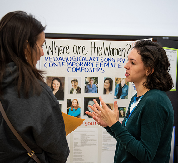 Two women stand in front of a presentation board. They are talking with each other. Two women stand in front of a presentation board. They are talking with each other.