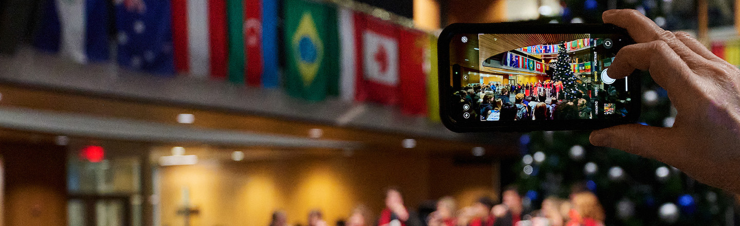 A mobile phone camera take a photo of a choir near a Christmas tree.