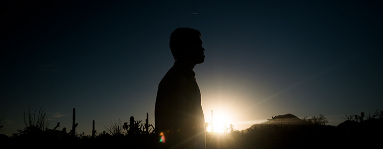 A student stands silhouetted against the sun A student stands silhouetted against the sun