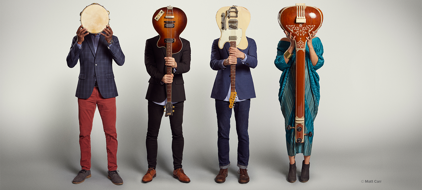 American Patchwork Quilt posed with the body of their instruments in front of their faces with the instruments neck toward the ground. 