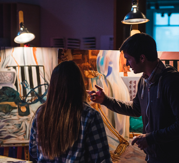 An art teacher points out something on a students painting