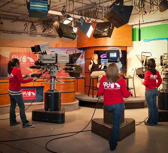Broadcast journalism students recording video in a news studio setting. Broadcast journalism students recording video in a news studio setting.